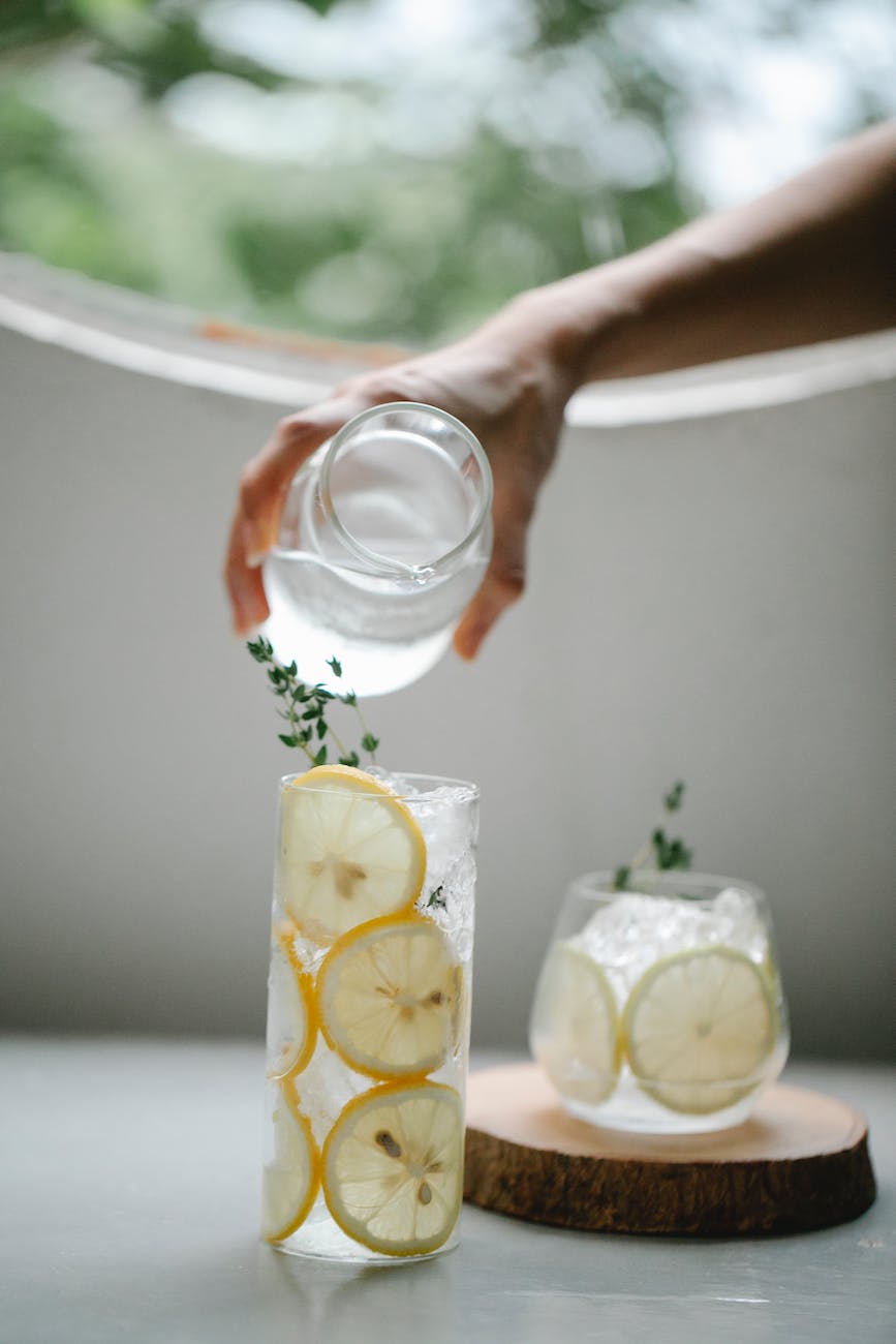 crop person pouring water into lemon drink