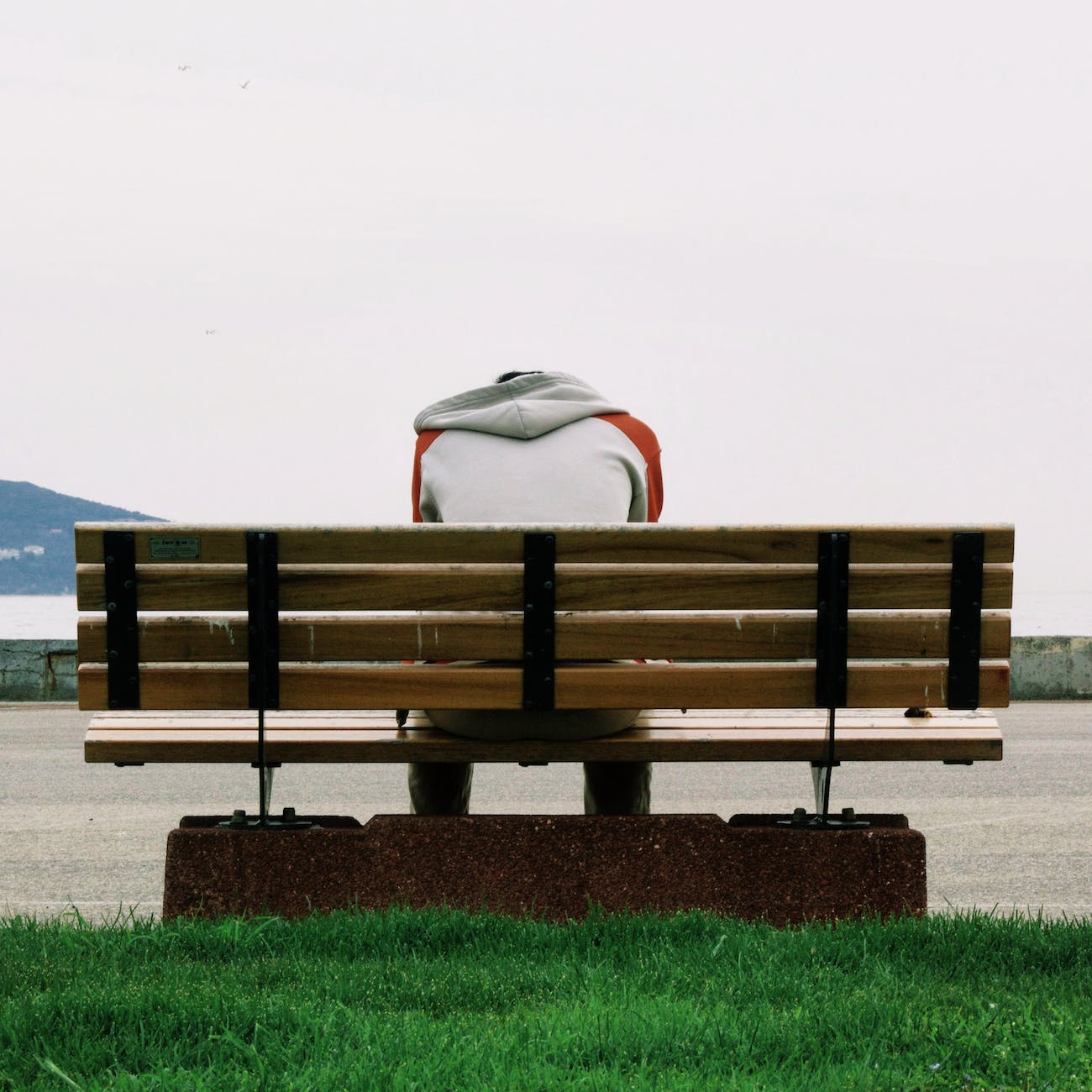 person wearing grey and orange hoodie sitting on brown wooden park bench during daytime